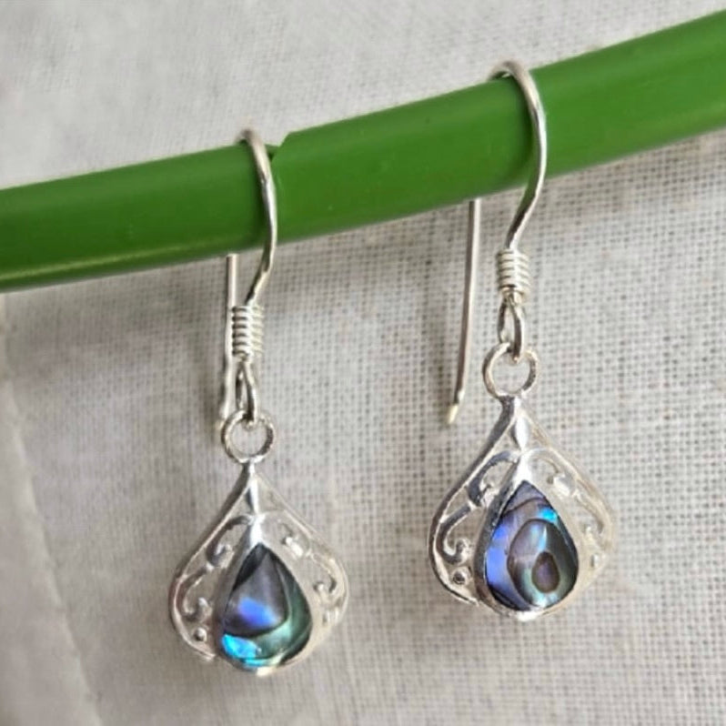 Silver earrings with blue gemstones hanging on a green rod against a light background