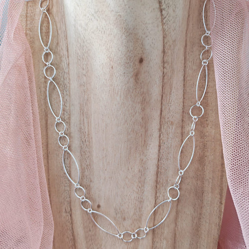 Silver chain necklace on a wooden surface with pink fabric
