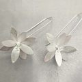 A pair of sterling silver long drop earrings with a floral design, displayed against a textured grey background.