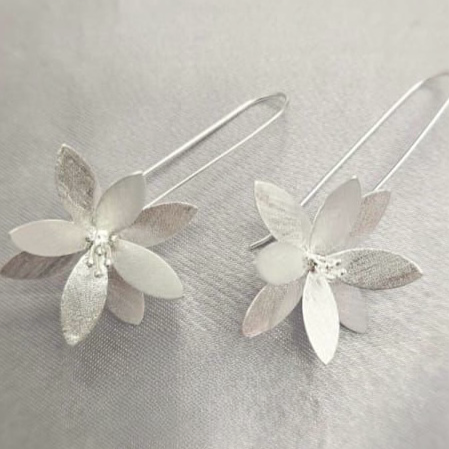 A pair of sterling silver long drop earrings with a floral design, displayed against a textured grey background.