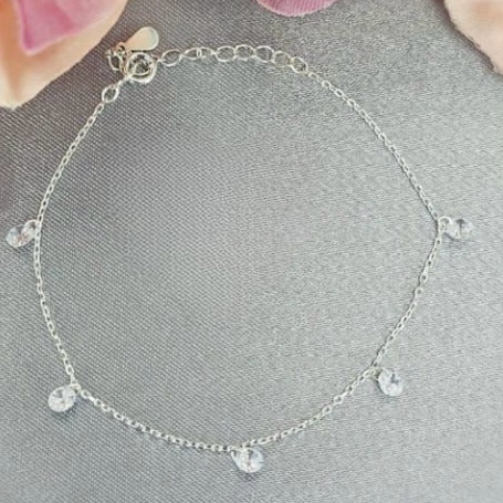 A sterling silver bracelet with dangling cubic zirconia crystals on achain, displayed against a floral background.