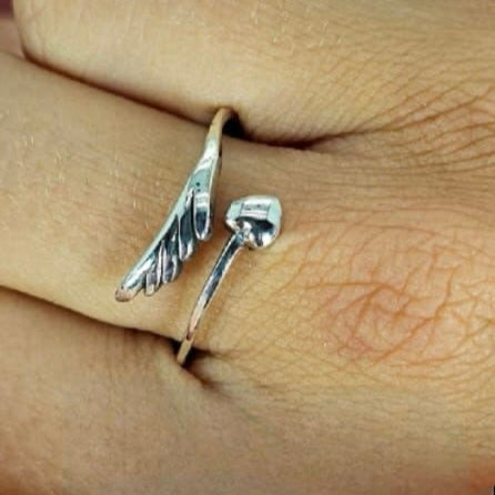 A sterling silver ring with a heart and wing design, displayed on a person's finger.