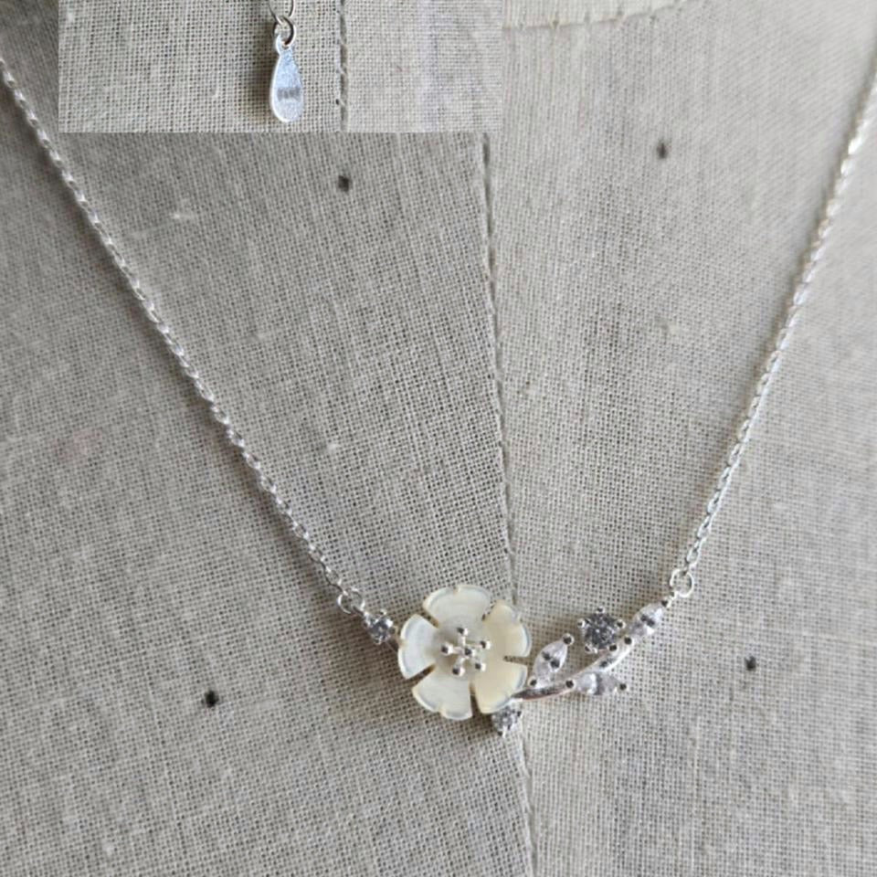 Silver necklace with a floral pendant on a textured fabric background