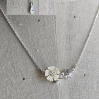 Silver necklace with a floral pendant on a textured fabric background