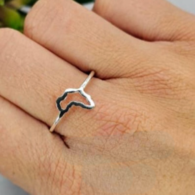 A person's hand wearing a silver ring with an Africa-shaped outline design.