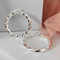 Silver hoop earrings on a light gray surface with a pink fabric background