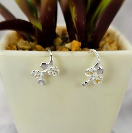 Silver flower drop earrings hanging from short stems, displayed in a white vase with a green plant background.