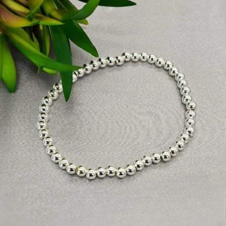 A silver ball bracelet on an elastic band, displayed alongside green foliage.
