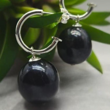 Silver hoop earrings with black beads on a green leaf background