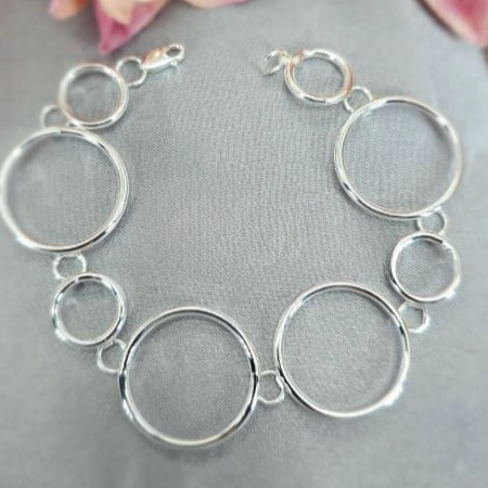 A sterling silver bracelet with a series of connected circles, displayed on a textured background with flower accents.