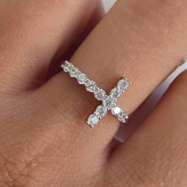 Silver cross-shaped ring with clear stones on a finger