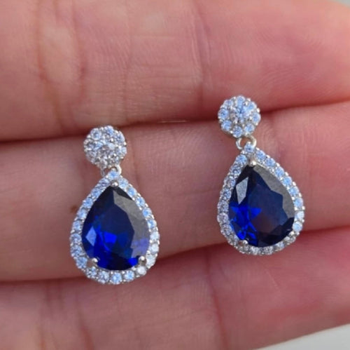 Teardrop-shaped blue gemstone earrings with silver accents on a hand.