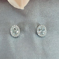 A pair of sterling silver and cubic zirconia oval stud earrings displayed on a fabric surface, with a pink floral petal in the background.
