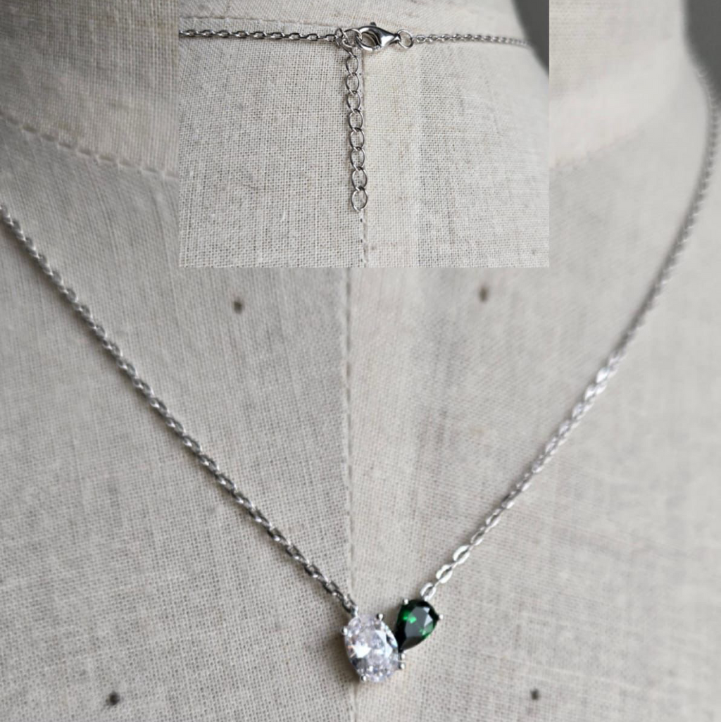 Necklace with a green gemstone and clear stone on a light gray background