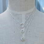 Three silver necklaces with circular pendants on a mannequin.