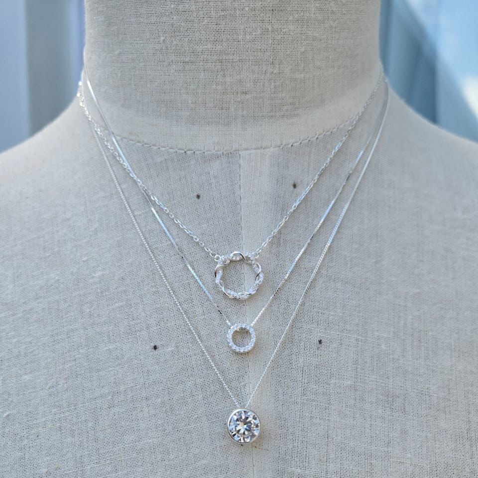 Three silver necklaces with circular pendants on a mannequin.
