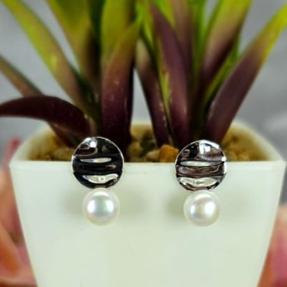 A pair of sterling silver round disc earrings with freshwater pearls, displayed in a white vase with green leaves.