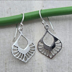 Silver earrings hanging from a green rod on a textured surface
