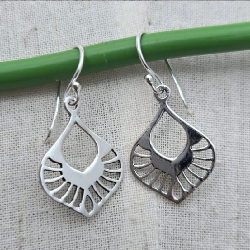 Silver earrings hanging from a green rod on a textured surface