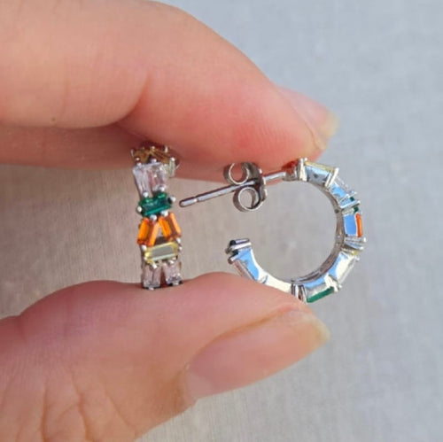 Close-up of two pairs of earrings held between fingers against a neutral background