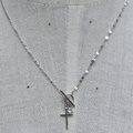 Silver necklace with a cross pendant on a gray fabric background