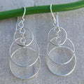 Genuine sterling silver hoop earrings hanging on a green stick against a grey background