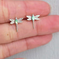 Silver dragonfly-shaped earrings with gemstones on a hand