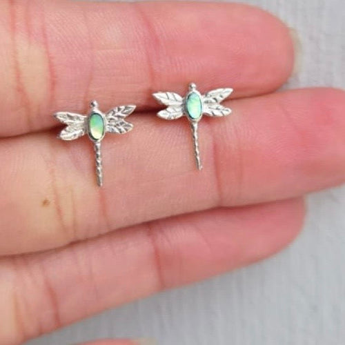Silver dragonfly-shaped earrings with gemstones on a hand