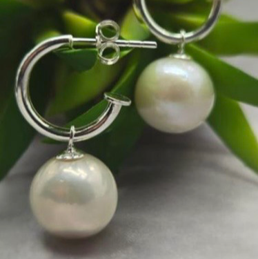 Pearl earrings with silver hoops on a green leaf background