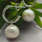 Pearl earrings with silver hoops on a green leaf background