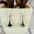A pair of sterling silver triangle drop earrings hanging from a hook, displayed in front of a potted plant.