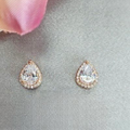 A pair of teardrop-shaped cubic zirconia earrings with rose gold plating, displayed against a neutral background with a pink floral element.