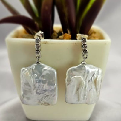 A pair of square freshwater pearl earrings with cubic zirconia on the stems, displayed in a white vase with a green plant.