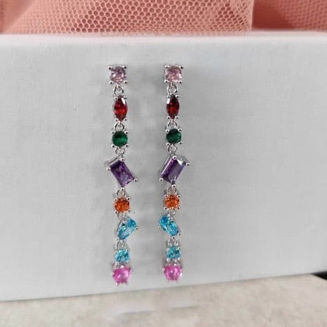 Multicolored gemstone earrings on a white card with a pink fabric background