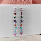 Multicolored gemstone earrings on a white card with a pink fabric background
