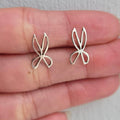 Silver butterfly earrings held between fingers on a neutral background