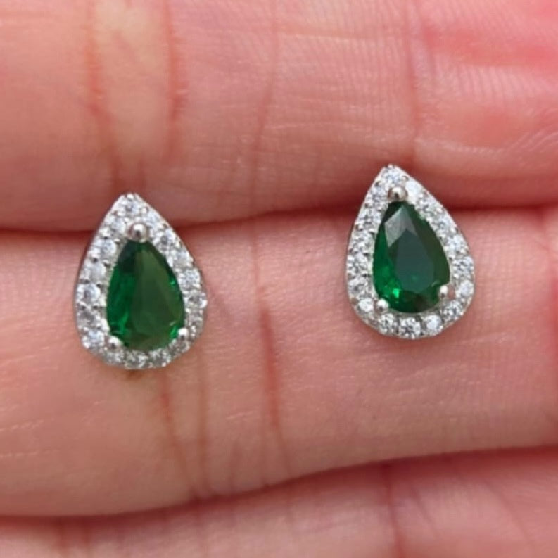 Teardrop-shaped emerald earrings with silver settings on a hand.