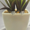 A pair of silver stud earrings designed in the shape of a tree of life, displayed in a white pot with green artificial turf.