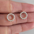 Silver beaded circle earrings held between fingers on a neutral background