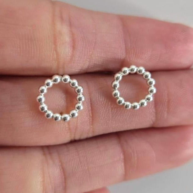 Silver beaded circle earrings held between fingers on a neutral background