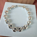 Silver chain bracelet on a white card with a wooden surface in the background