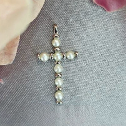 A silver cross pendant with freshwater pearl accents placed on a textured surface with a blurred background.