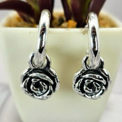 A pair of sterling silver hoop earrings with rose charms, displayed on a table next to a potted plant.
