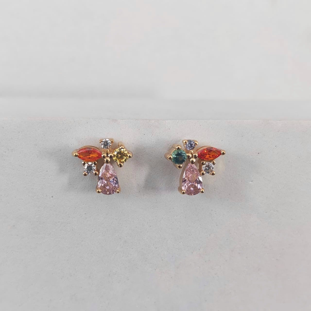 Pair of earrings with colorful gemstones on a light gray background