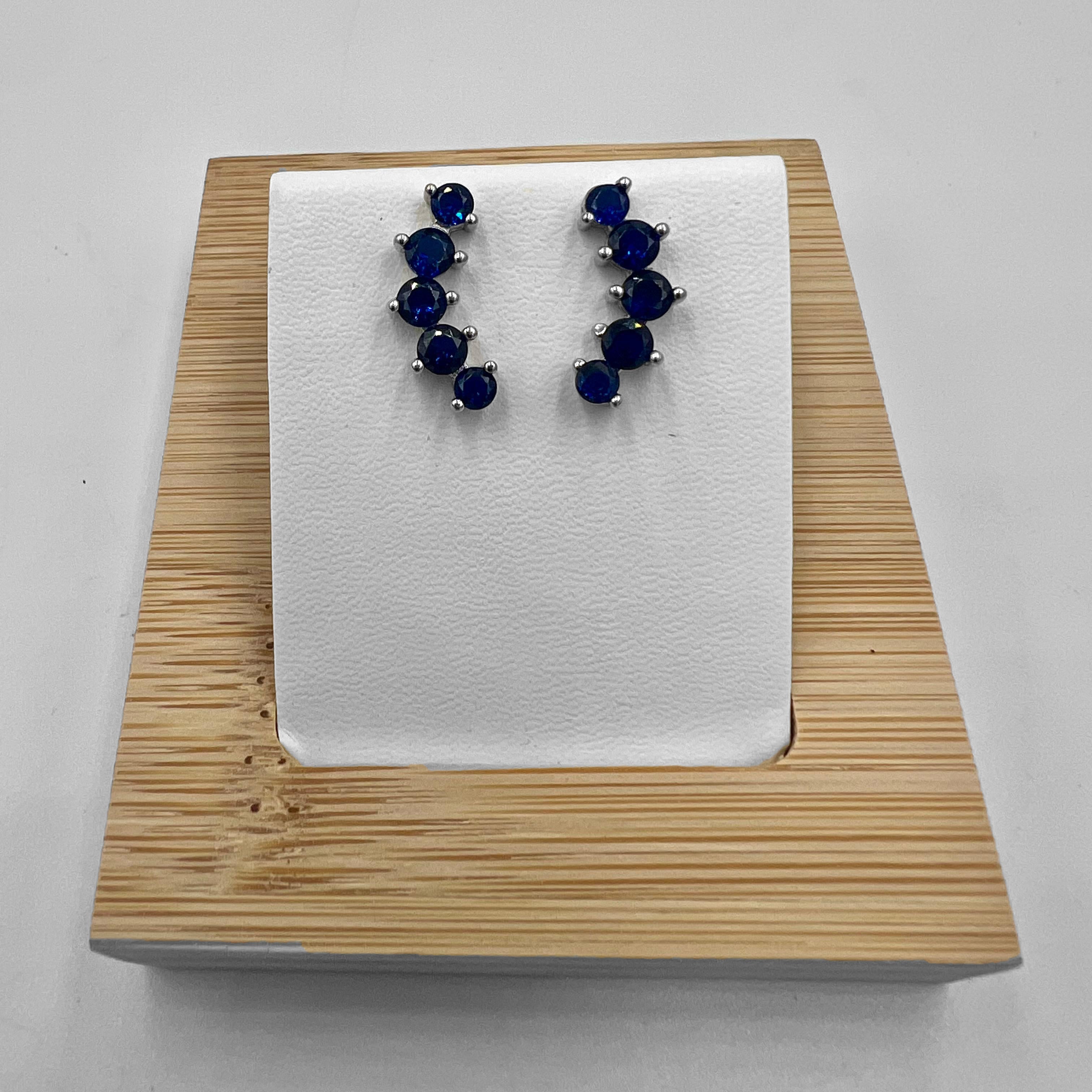 A pair of blue stone earrings crafted from sterling silver, displayed on a white mount and wooden base.