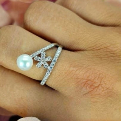 A sterling silver V shape ring with cubic zirconia and a freshwater pearl detail, displayed on a person's finger.