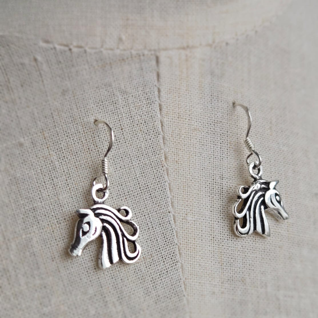 Silver horse head earrings on a textured beige background