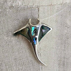 Silver pendant with abalone shell inlay on a textured fabric background