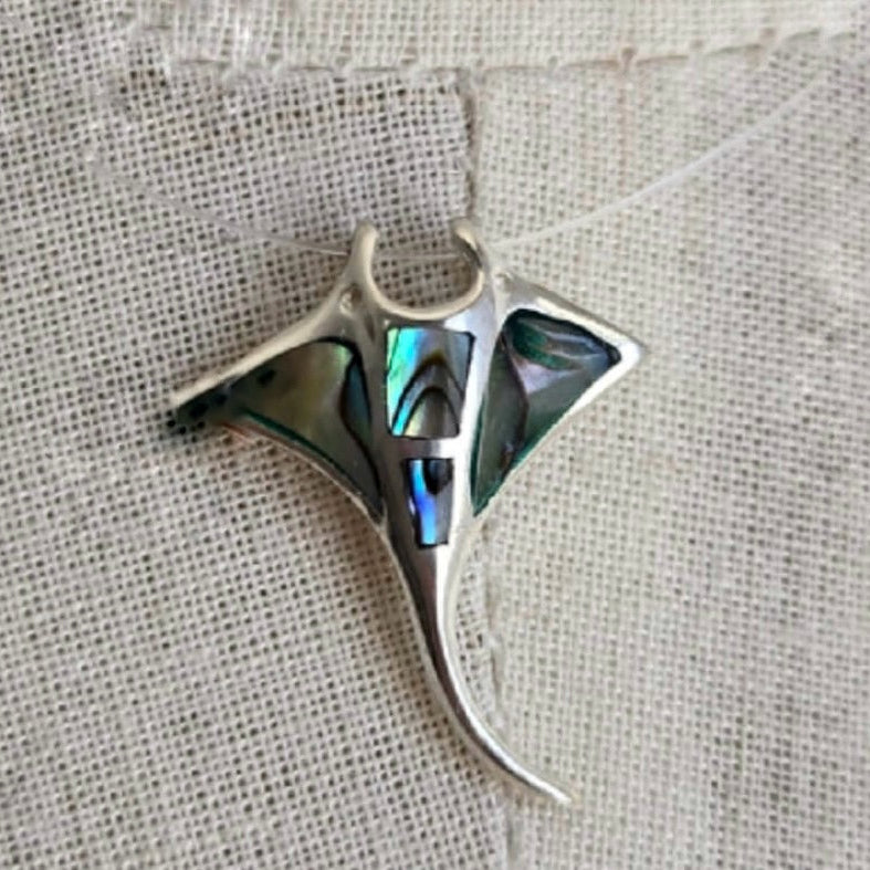 Silver pendant with abalone shell inlay on a textured fabric background