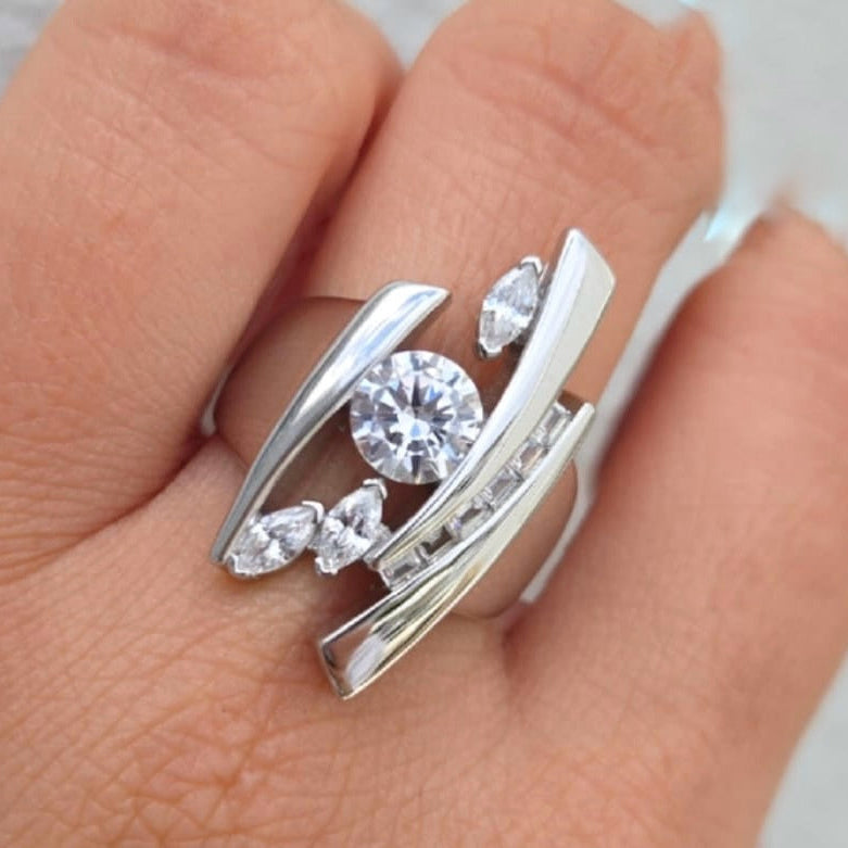 Silver ring with gemstones on a finger against a neutral background